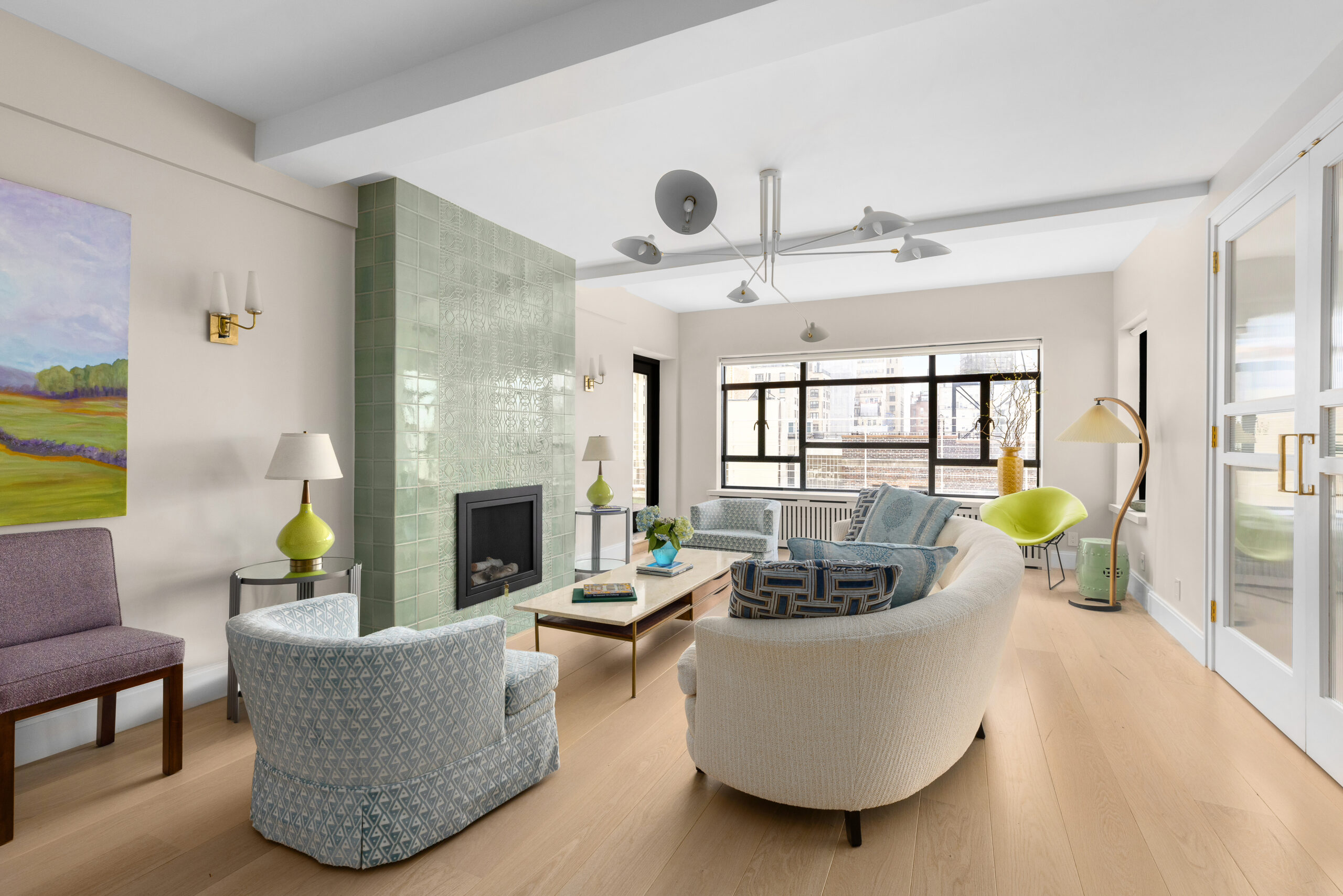 Full apartment remodel Upper West Side living room featuring green tiled fireplace, curved seating, and large casement windows overlooking the city.