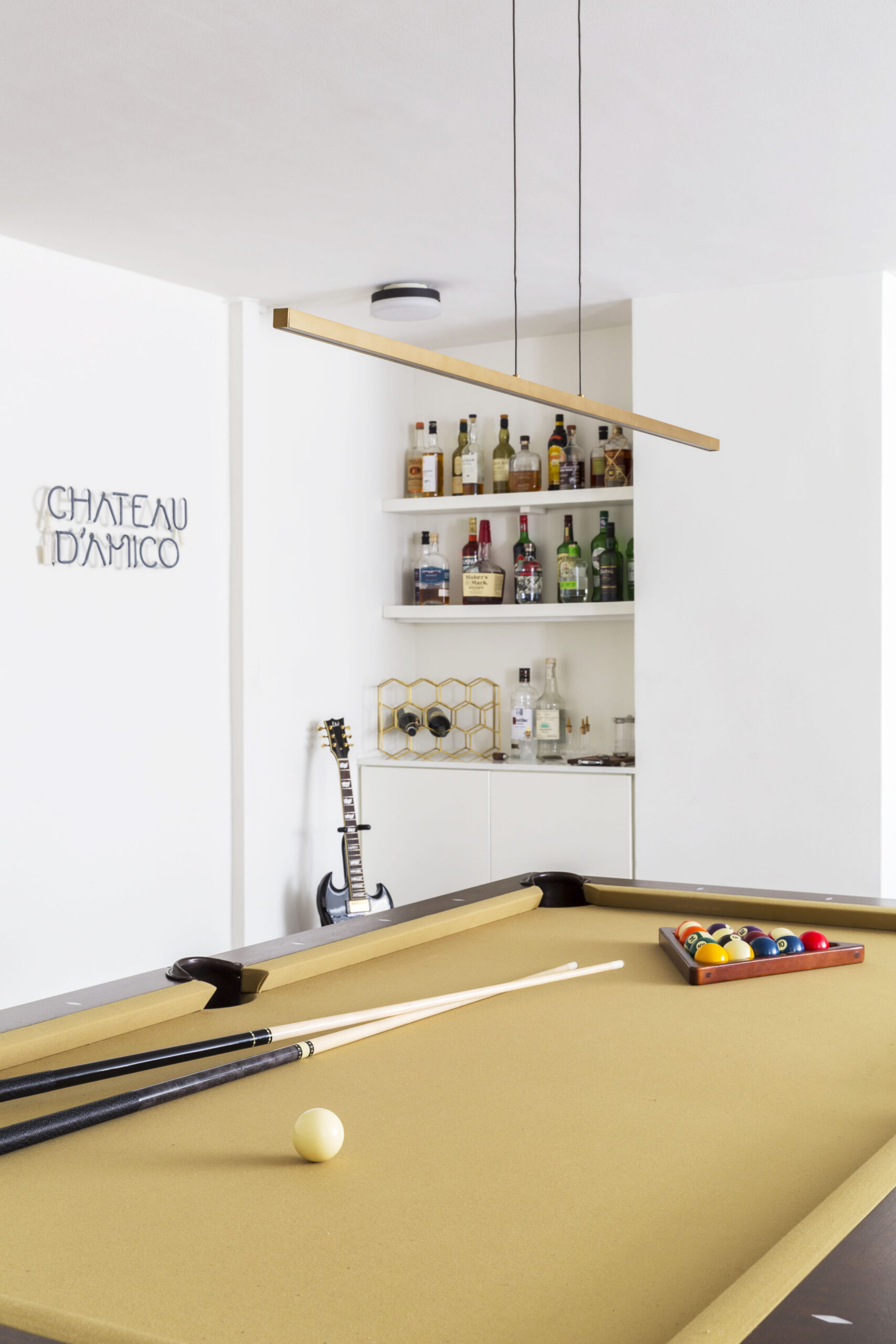 Pool table with hanging light, dry bar with liquor, and electric guitar in the corner