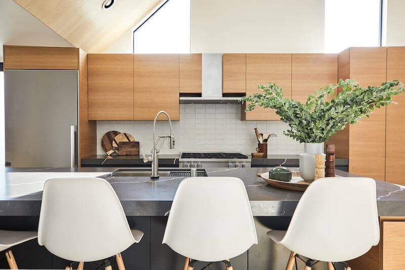 Contemporary kitchen with warm wood cabinets, stainless appliances, charcoal stone counters, and island seating under a vaulted ceiling.