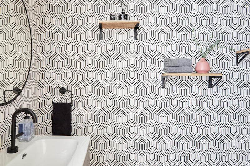 Powder room accent wall with graphic wallpaper, open wood shelves with decor and towels, and matching black metal brackets and fixtures.