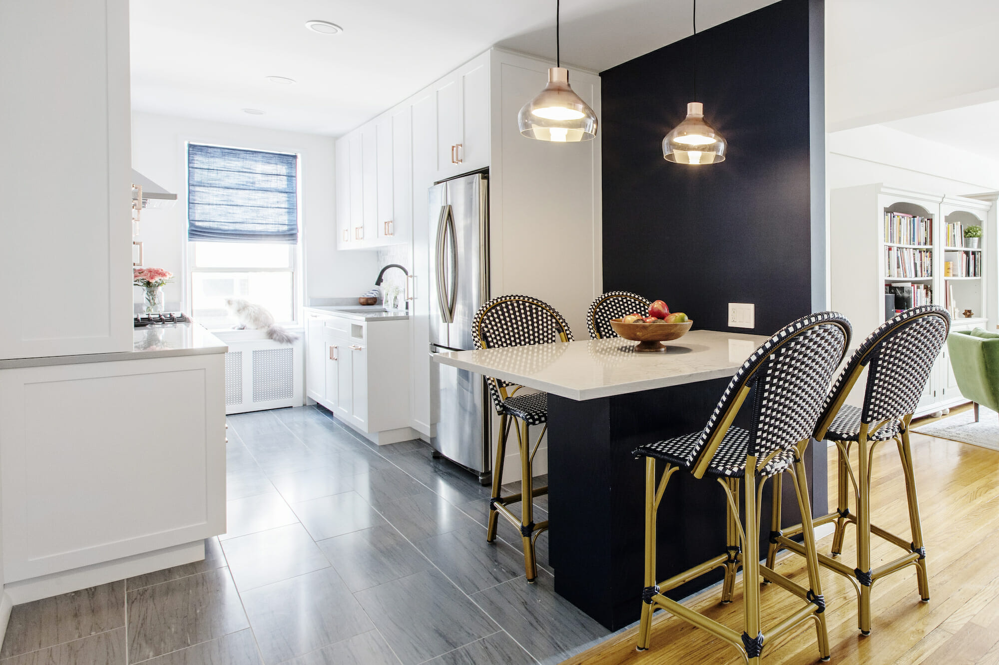 Renovated open kitchen in Bronx with white cabinets, stainless fridge, peninsula for three, pendant lights, and a blue Roman shade.