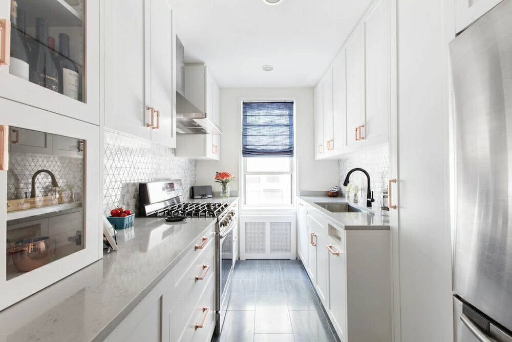 Bright white galley kitchen with shaker cabinets, copper pulls, quartz counters, geometric tile, and blue Roman shade after Bronx kitchen renovation.
