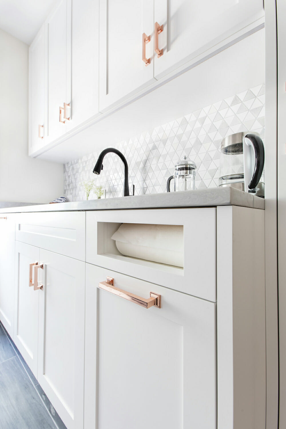 Sink run with pull-down faucet, quartz top, paper-towel niche, shaker cabinets, and copper hardware after Bronx kitchen remodel.